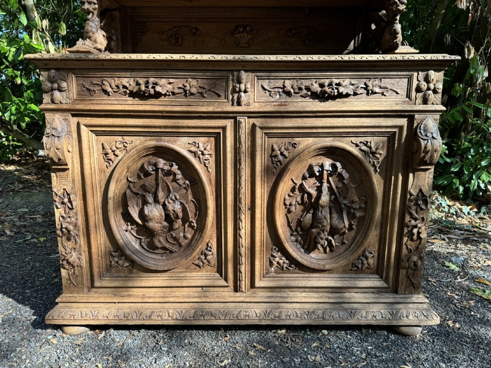 A two-piece bleached oak hunting cabinet featuring hand-carved relief panels of game birds, glazed upper doors, and a decorative mask pediment. View III