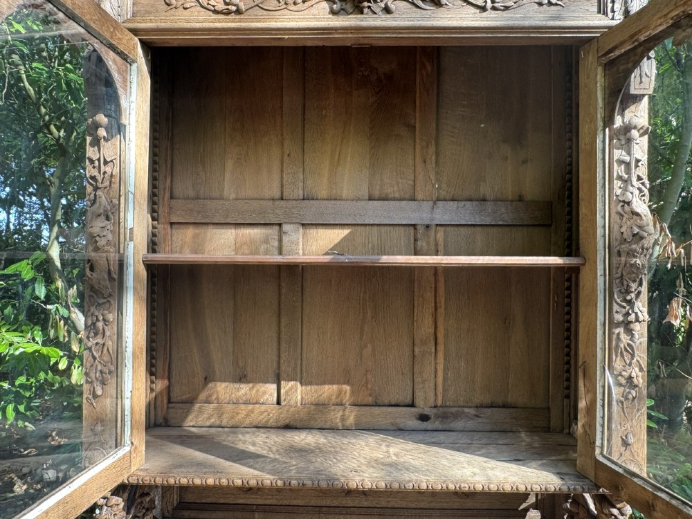 A two-piece bleached oak hunting cabinet featuring hand-carved relief panels of game birds, glazed upper doors, and a decorative mask pediment. View X