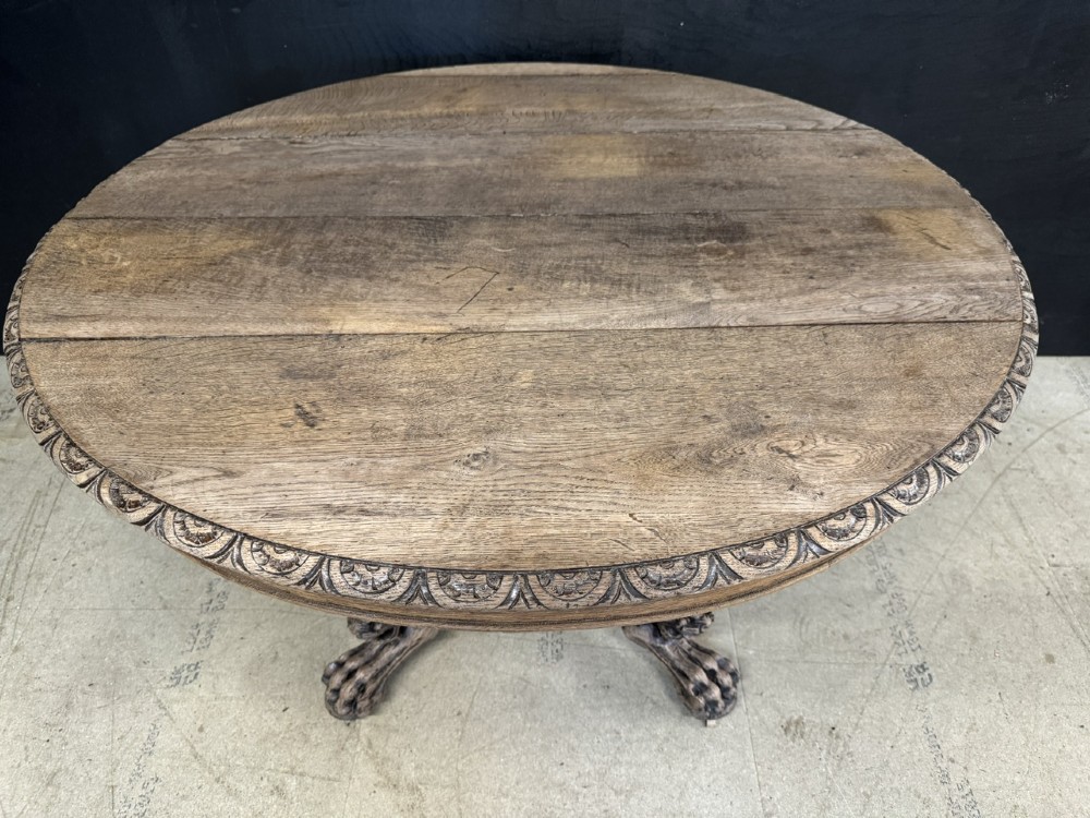 A round bleached oak dining table featuring an intricately carved apron and a central pedestal supported by four beast-head scrolled legs. View II