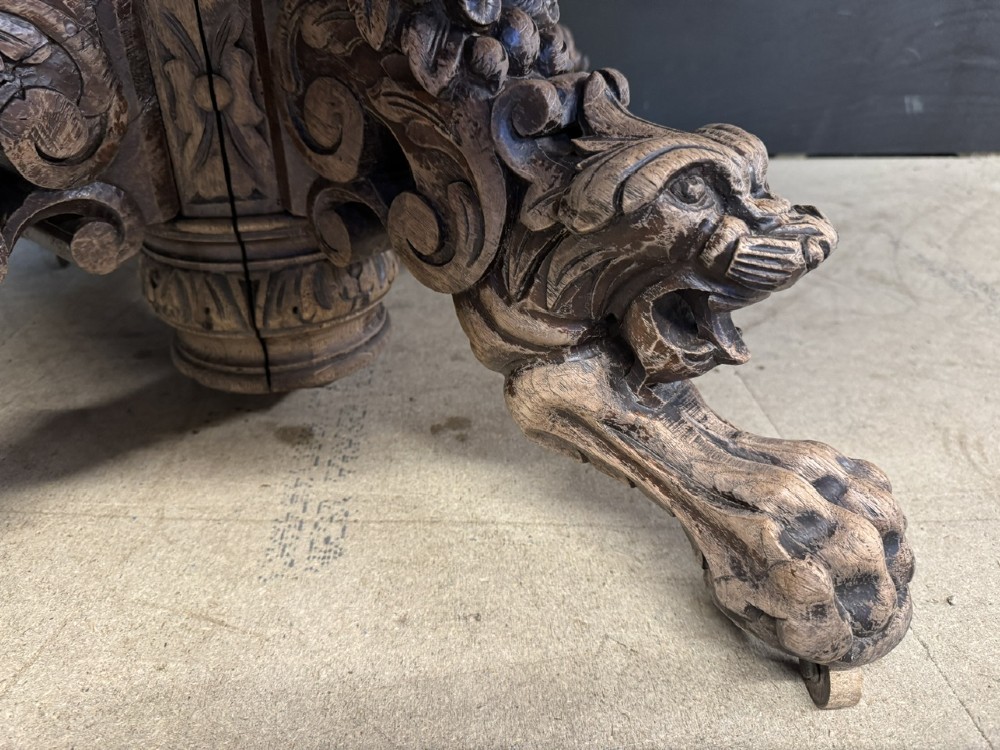 A round bleached oak dining table featuring an intricately carved apron and a central pedestal supported by four beast-head scrolled legs. View VII