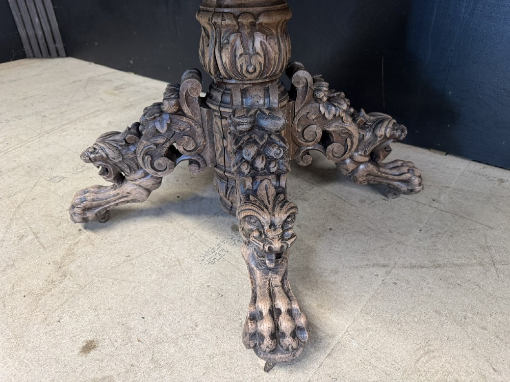 A round bleached oak dining table featuring an intricately carved apron and a central pedestal supported by four beast-head scrolled legs. View IX
