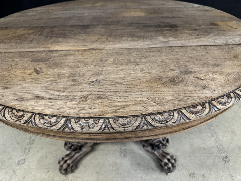 A round bleached oak dining table featuring an intricately carved apron and a central pedestal supported by four beast-head scrolled legs. View XI