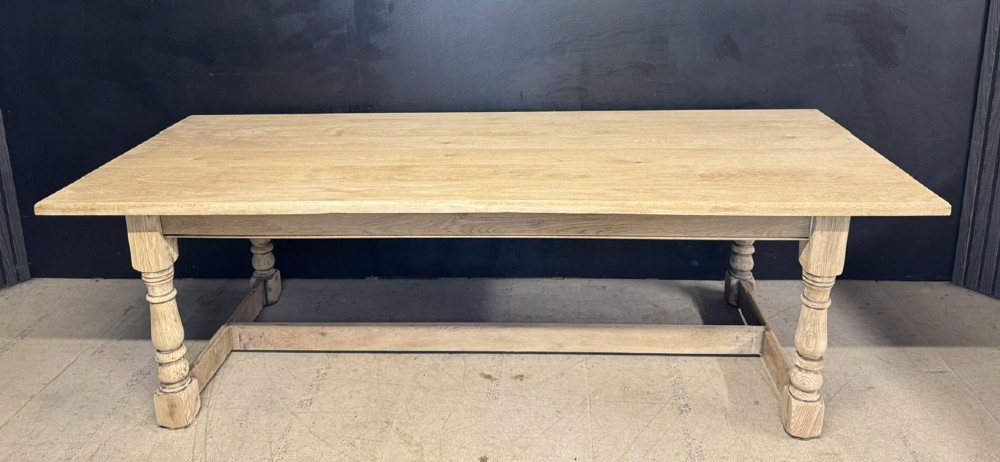 A large light oak farmhouse dining table featuring a solid plank top, turned legs, and an H-shaped stretcher base.