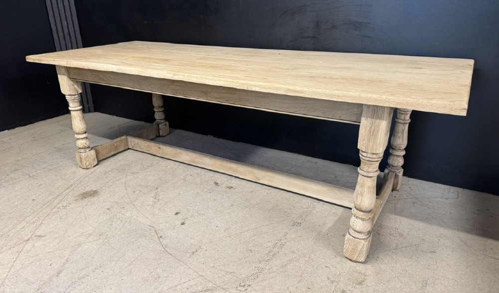 A large light oak farmhouse dining table featuring a solid plank top, turned legs, and an H-shaped stretcher base. View III