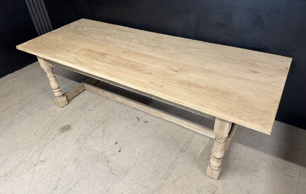 A large light oak farmhouse dining table featuring a solid plank top, turned legs, and an H-shaped stretcher base. View IV