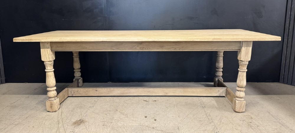 A large light oak farmhouse dining table featuring a solid plank top, turned legs, and an H-shaped stretcher base. View V