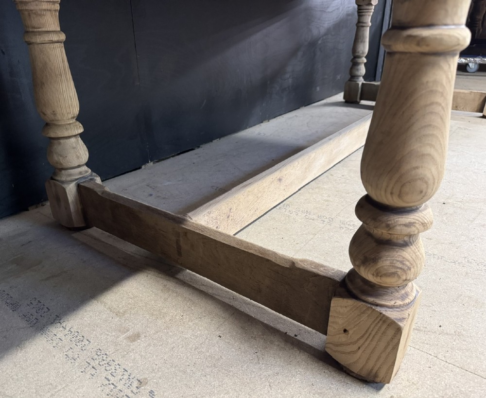 A large light oak farmhouse dining table featuring a solid plank top, turned legs, and an H-shaped stretcher base. View XI