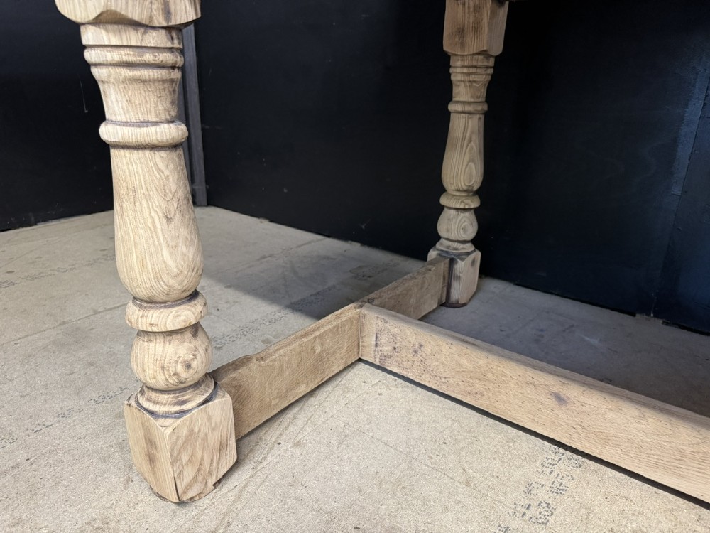 A large light oak farmhouse dining table featuring a solid plank top, turned legs, and an H-shaped stretcher base. View XIII