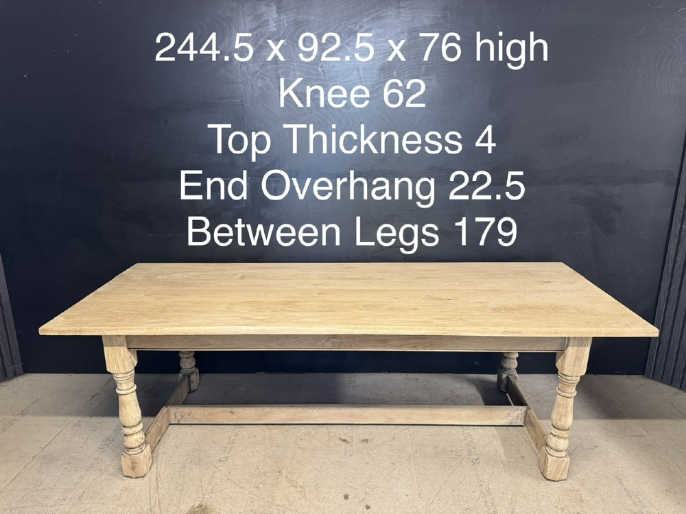 A large light oak farmhouse dining table featuring a solid plank top, turned legs, and an H-shaped stretcher base. View XV