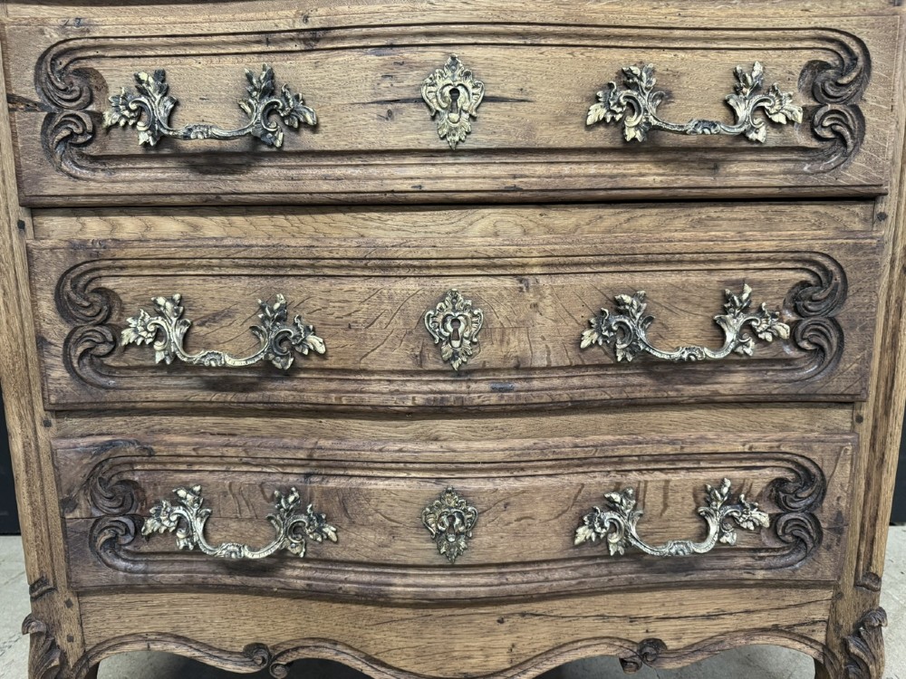 A French provincial bleached oak commode featuring three drawers with carved decorative mouldings and cast metal handles. View X