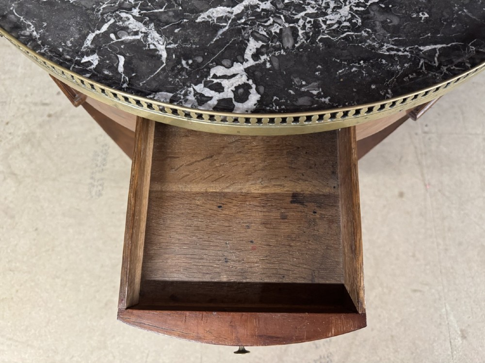 A circular French Louis XVI style lamp table featuring a dark veined marble top, a pierced brass gallery rim, a single drawer, and four square tapered legs. View VI