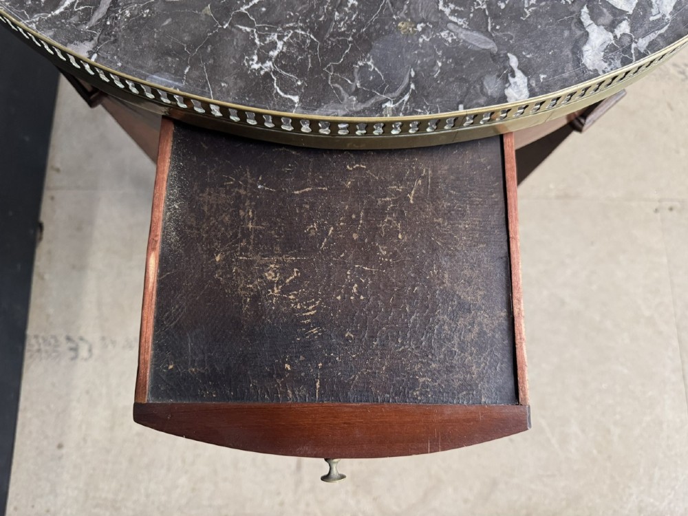 A circular French Louis XVI style lamp table featuring a dark veined marble top, a pierced brass gallery rim, a single drawer, and four square tapered legs. View VII