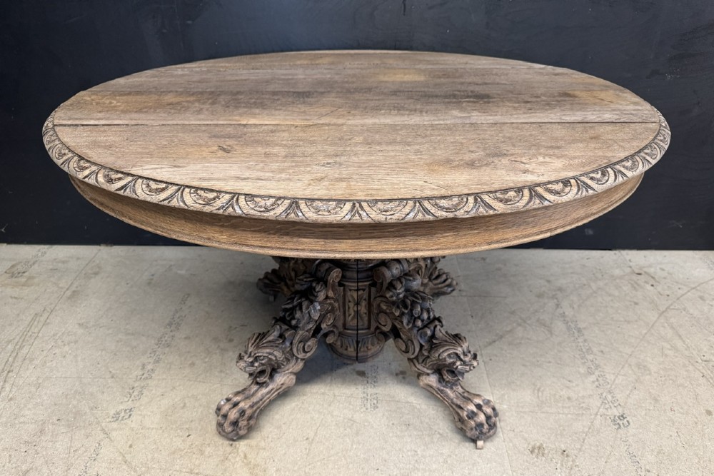 A circular French carved oak hunting table featuring an intricately carved rim and a central pedestal supported by carved lion head feet.