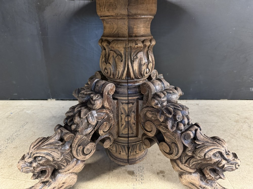 A circular French carved oak hunting table featuring an intricately carved rim and a central pedestal supported by carved lion head feet. View V