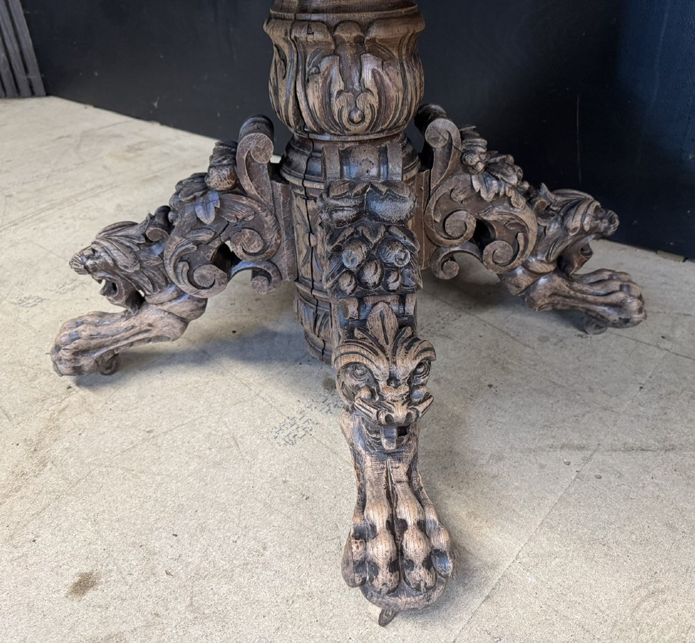 A circular French carved oak hunting table featuring an intricately carved rim and a central pedestal supported by carved lion head feet. View VIII