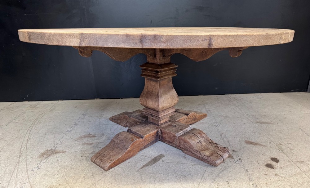 A large round oak dining table featuring a planked top and a substantial wooden cross-pedestal base. View IV