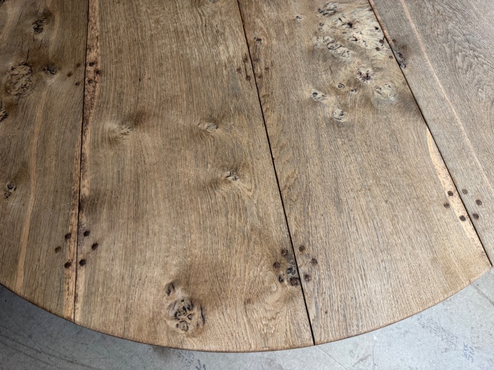 A large round oak dining table featuring a planked top and a substantial wooden cross-pedestal base. View IX