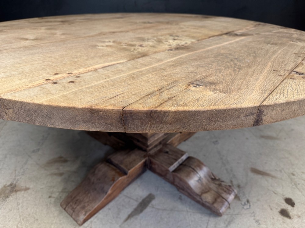 A large round oak dining table featuring a planked top and a substantial wooden cross-pedestal base. View X