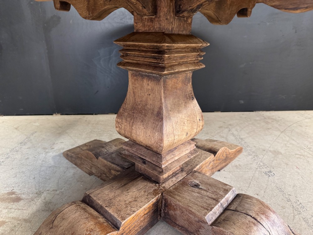 A large round oak dining table featuring a planked top and a substantial wooden cross-pedestal base. View XII