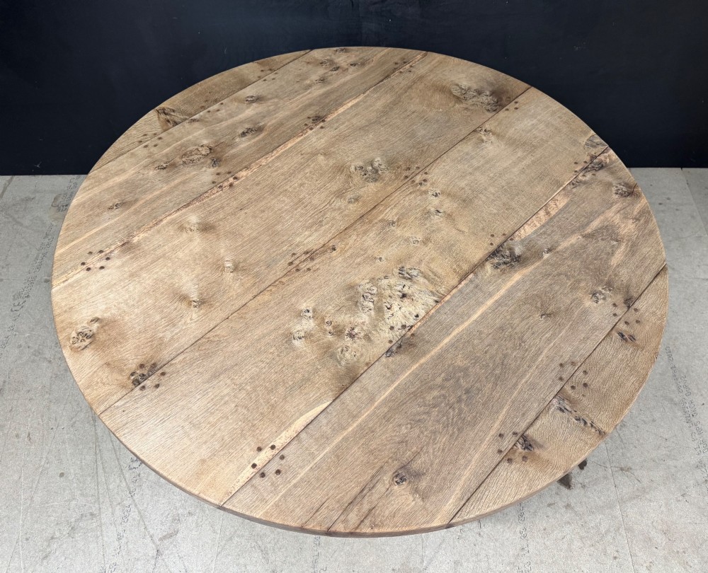A large round oak dining table featuring a planked top and a substantial wooden cross-pedestal base. View XIII