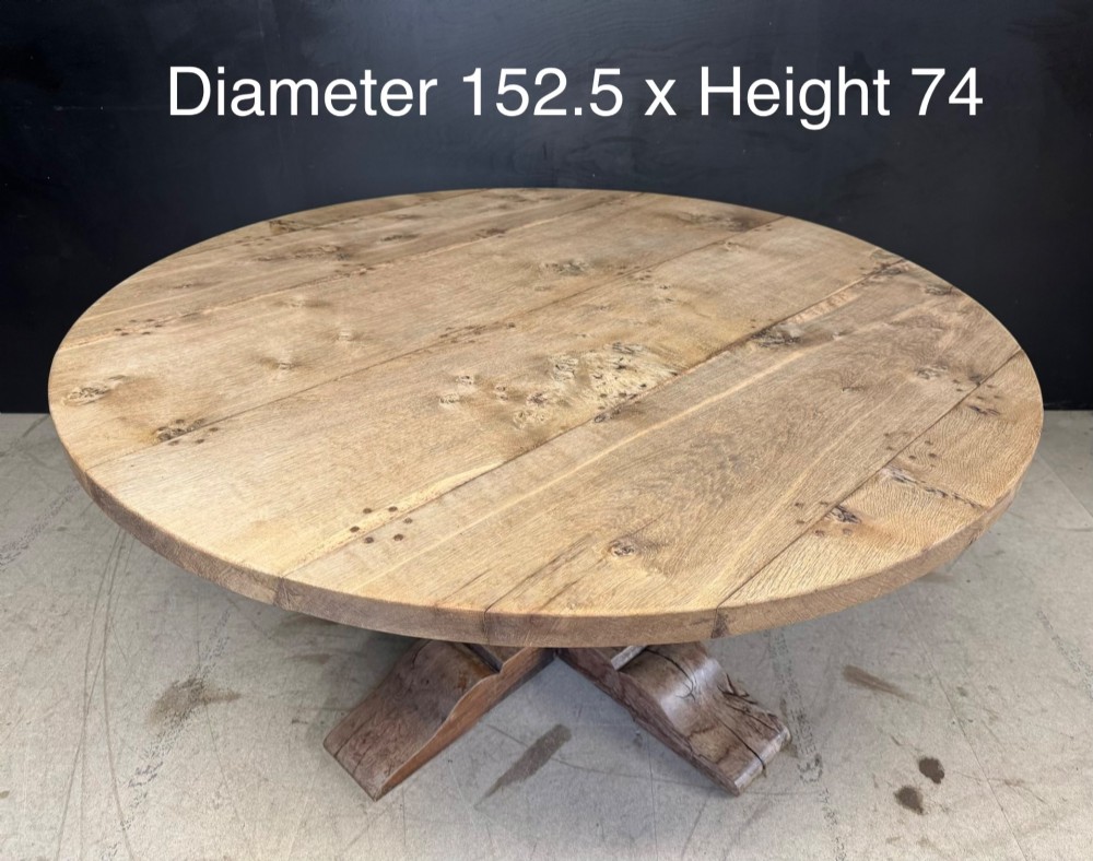 A large round oak dining table featuring a planked top and a substantial wooden cross-pedestal base. View XIV
