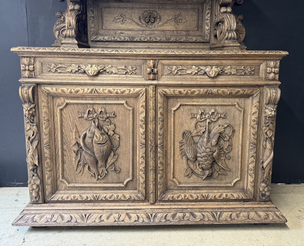A dark oak French hunting sideboard featuring a carved stag head top pediment, open middle shelves, and lower cabinet doors decorated with carved game birds. View II
