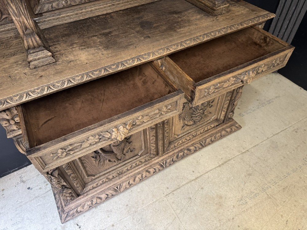 A dark oak French hunting sideboard featuring a carved stag head top pediment, open middle shelves, and lower cabinet doors decorated with carved game birds. View VI