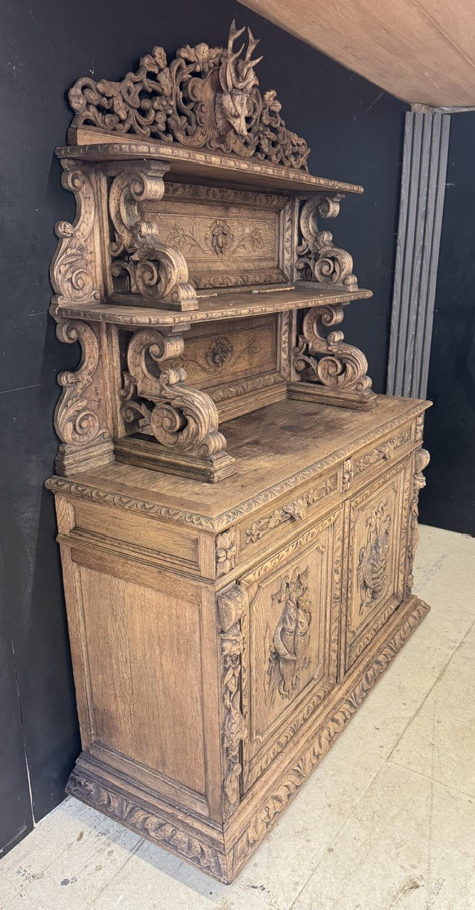 A dark oak French hunting sideboard featuring a carved stag head top pediment, open middle shelves, and lower cabinet doors decorated with carved game birds. View XII