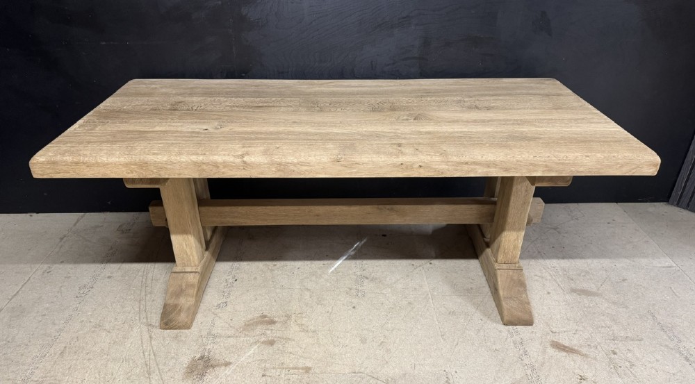 A solid bleached oak dining table featuring a thick rectangular top supported by a sturdy trestle base and central stretcher rail.