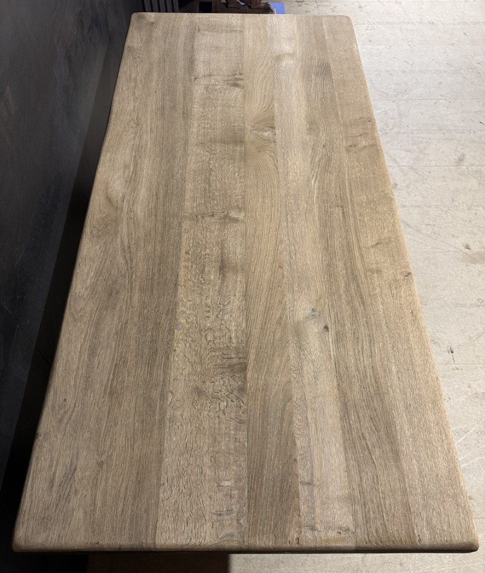 A solid bleached oak dining table featuring a thick rectangular top supported by a sturdy trestle base and central stretcher rail. View VI