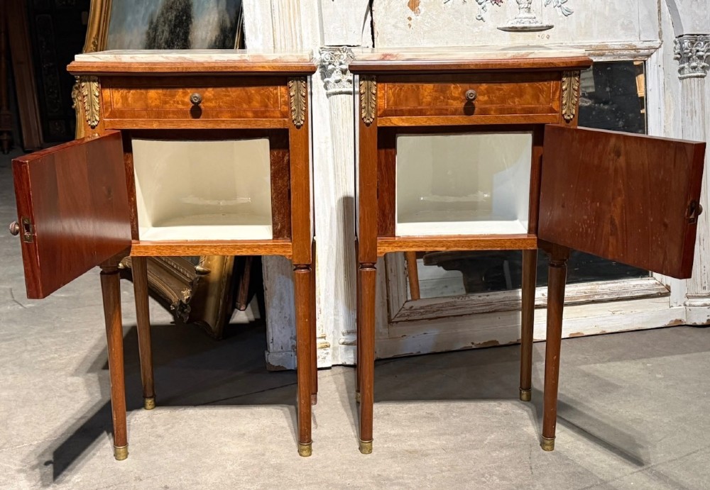A pair of French Louis XVI style wooden bedside cabinets featuring marble tops, single drawers, inlaid cupboard doors, and gilt brass mounts on slender tapered legs. View II