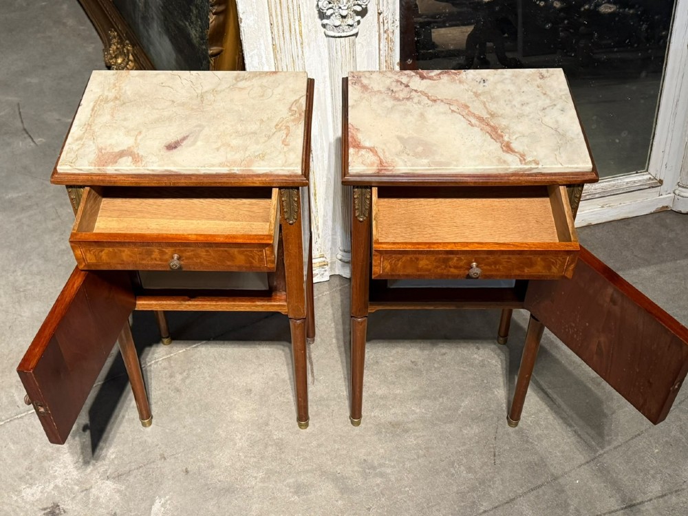 A pair of French Louis XVI style wooden bedside cabinets featuring marble tops, single drawers, inlaid cupboard doors, and gilt brass mounts on slender tapered legs. View VI