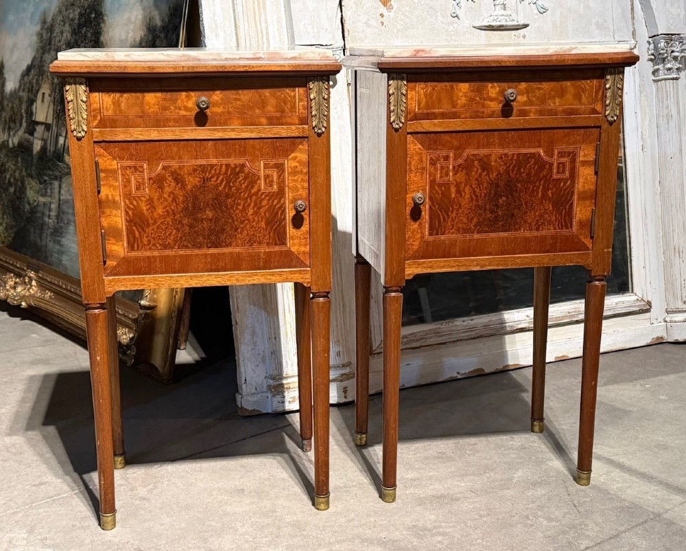 A pair of French Louis XVI style wooden bedside cabinets featuring marble tops, single drawers, inlaid cupboard doors, and gilt brass mounts on slender tapered legs. View IX