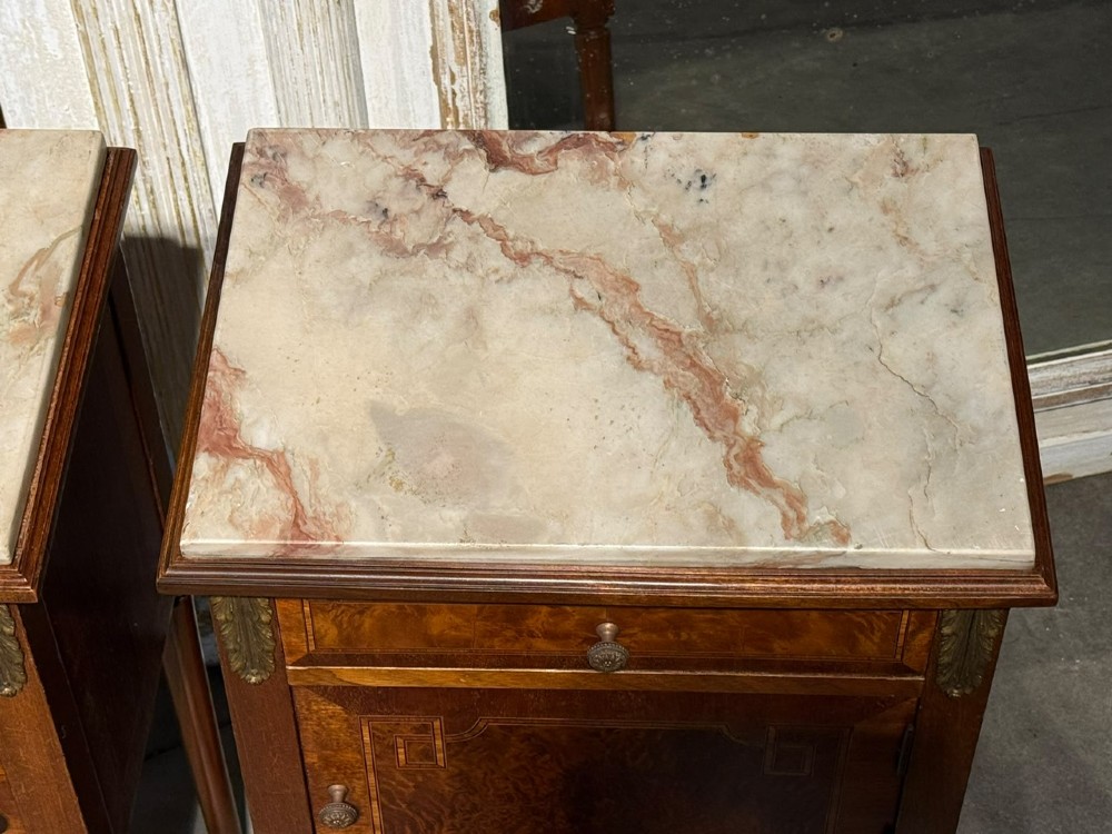 A pair of French Louis XVI style wooden bedside cabinets featuring marble tops, single drawers, inlaid cupboard doors, and gilt brass mounts on slender tapered legs. View X