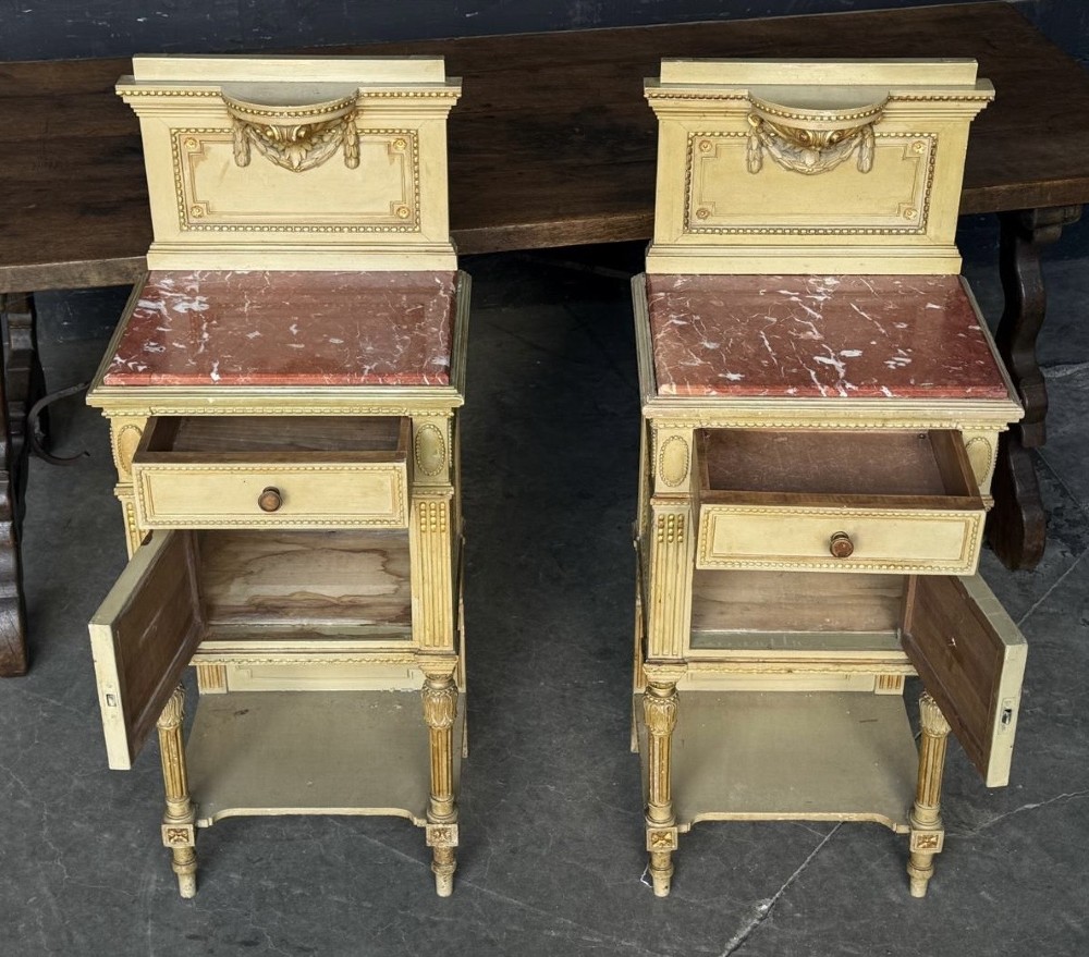 A matching pair of painted French neoclassical bedside cabinets featuring red marble tops, carved bracket superstructures, gold leaf detailing, drawers, and open lower shelves. View II