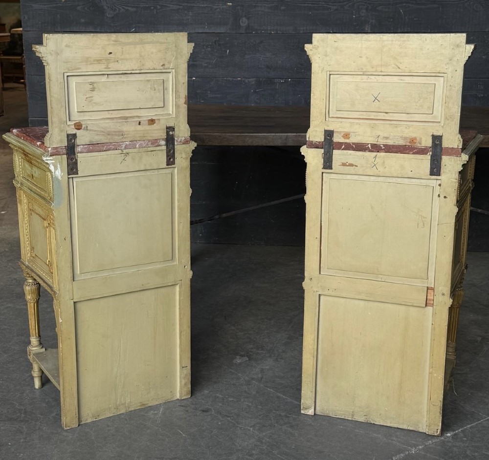 A matching pair of painted French neoclassical bedside cabinets featuring red marble tops, carved bracket superstructures, gold leaf detailing, drawers, and open lower shelves. View VI