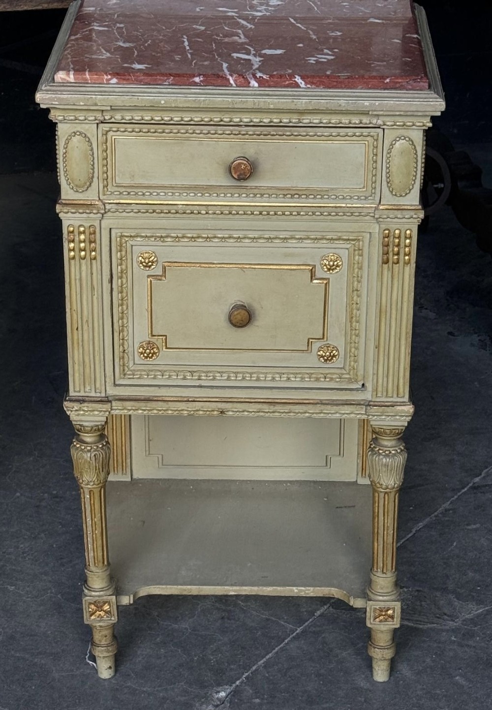 A matching pair of painted French neoclassical bedside cabinets featuring red marble tops, carved bracket superstructures, gold leaf detailing, drawers, and open lower shelves. View IX