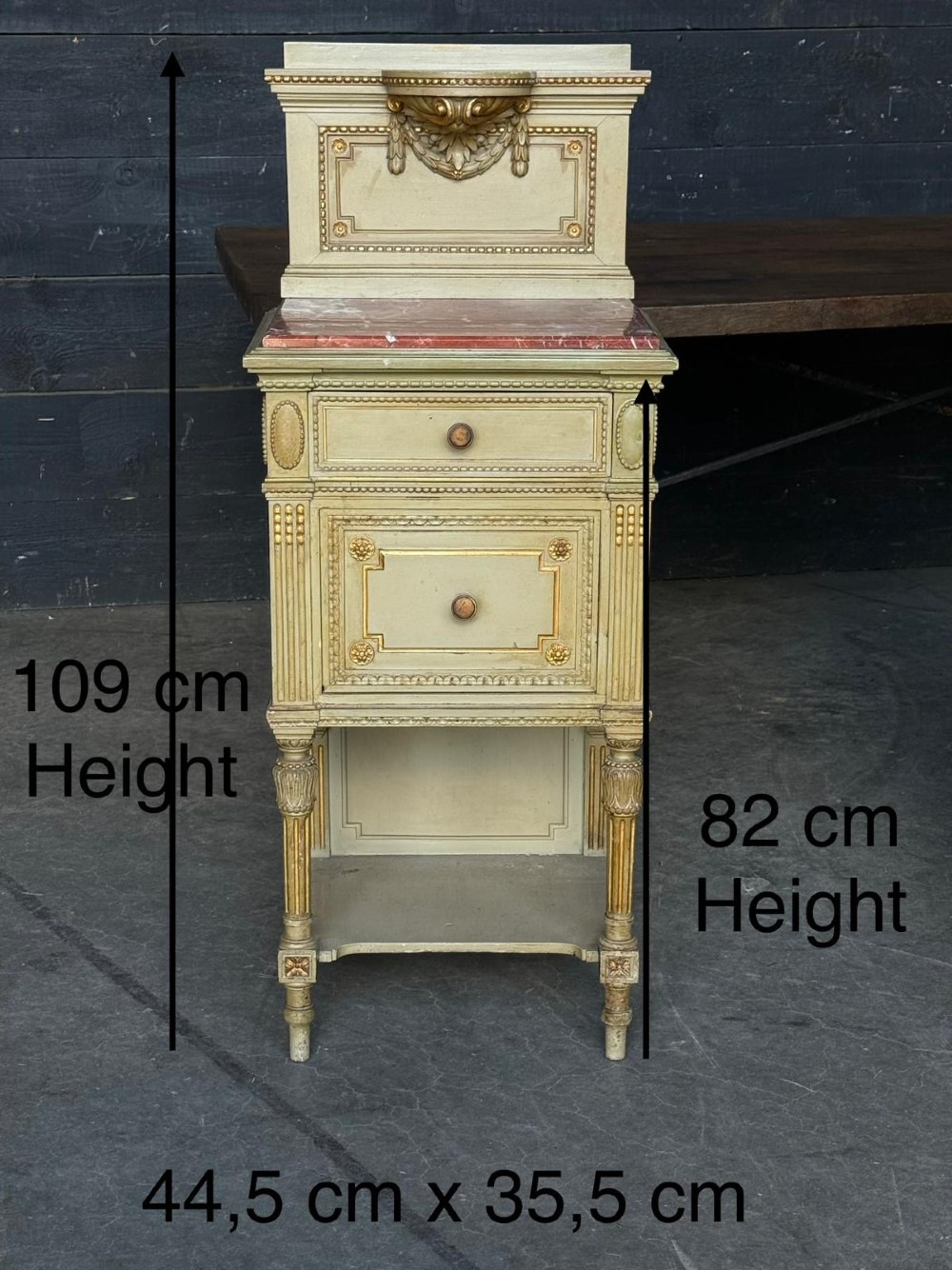 A matching pair of painted French neoclassical bedside cabinets featuring red marble tops, carved bracket superstructures, gold leaf detailing, drawers, and open lower shelves. View X