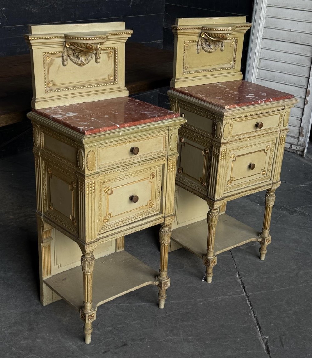 A matching pair of painted French neoclassical bedside cabinets featuring red marble tops, carved bracket superstructures, gold leaf detailing, drawers, and open lower shelves. View XI