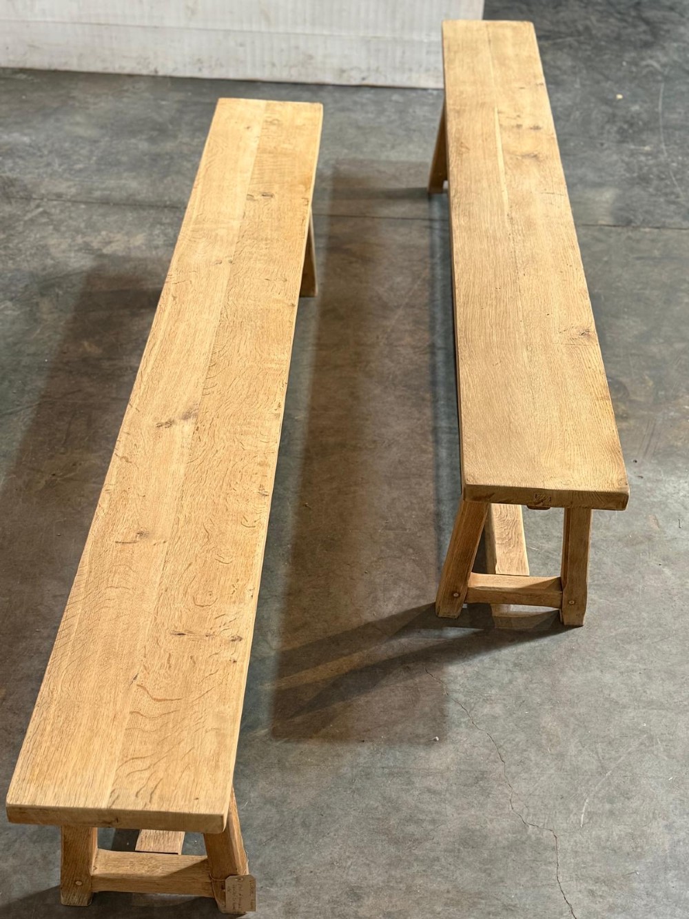 A pair of long rustic light oak dining benches with A-frame legs and cross-stretchers. View VII