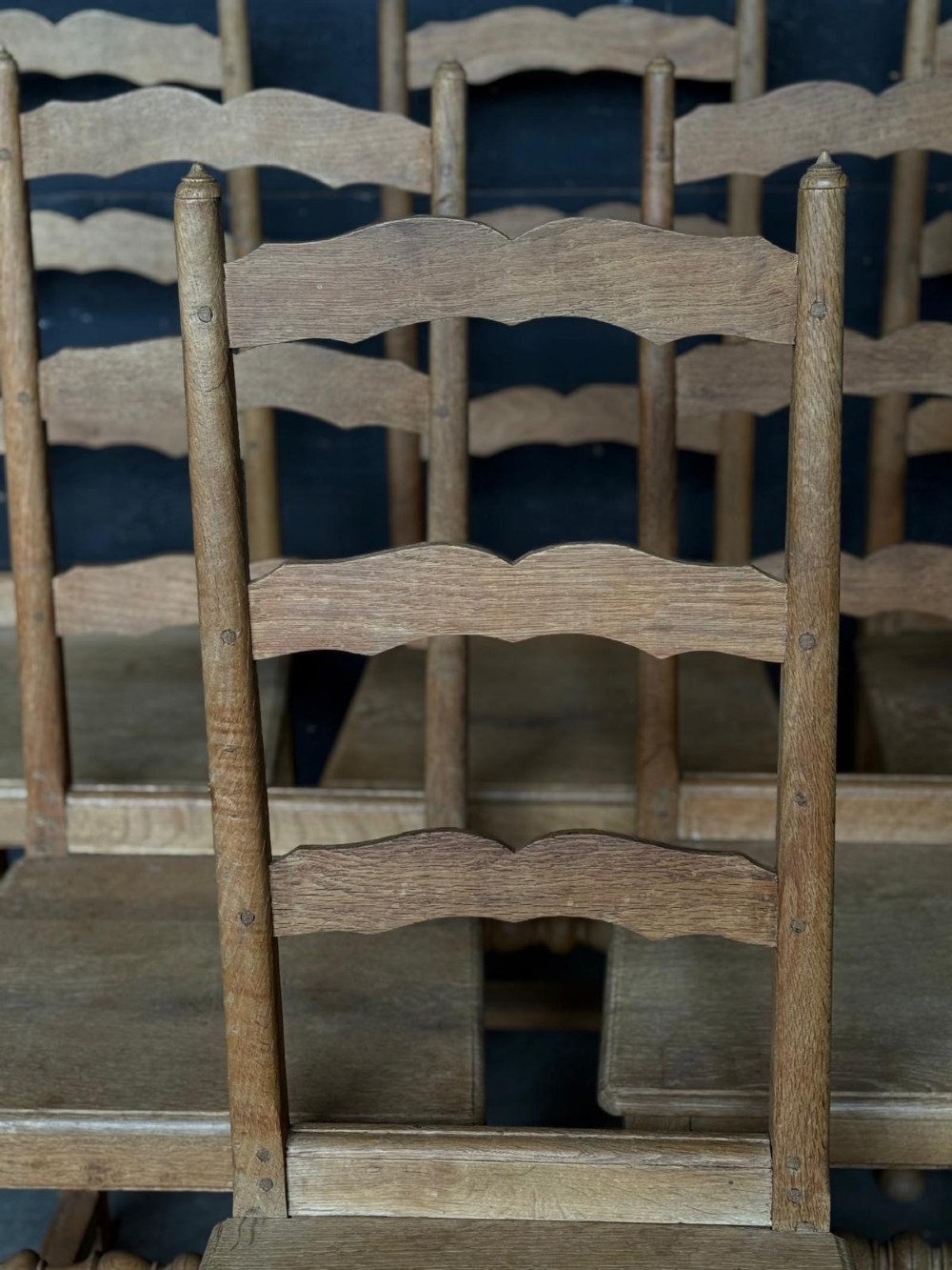 A set of six light oak ladderback dining chairs featuring wavy back slats, turned legs, and solid wooden seats. View VI