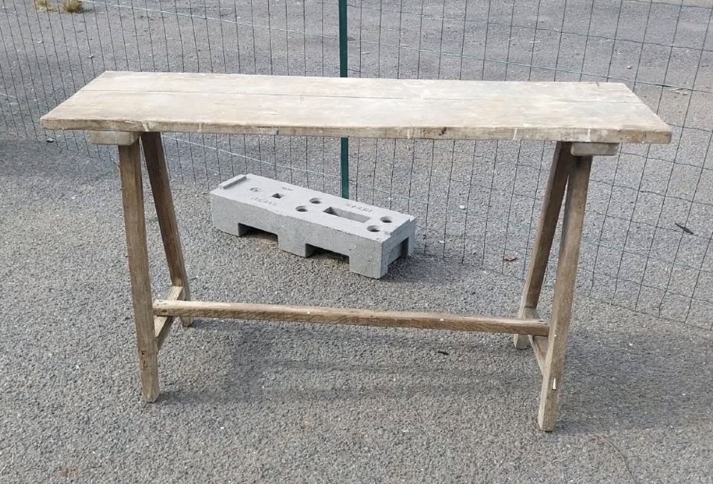 A rustic weathered wooden French laundry table featuring a plank top supported by angled A-frame trestle legs and a central stretcher. View II