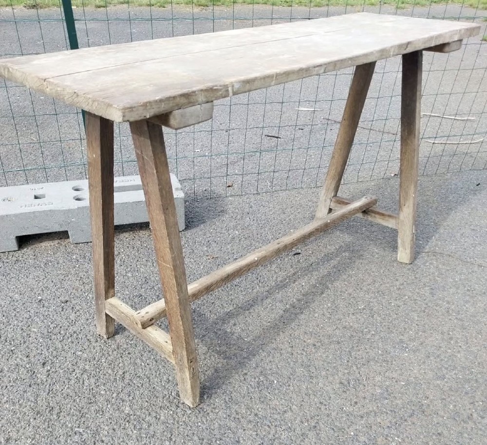 A rustic weathered wooden French laundry table featuring a plank top supported by angled A-frame trestle legs and a central stretcher. View III