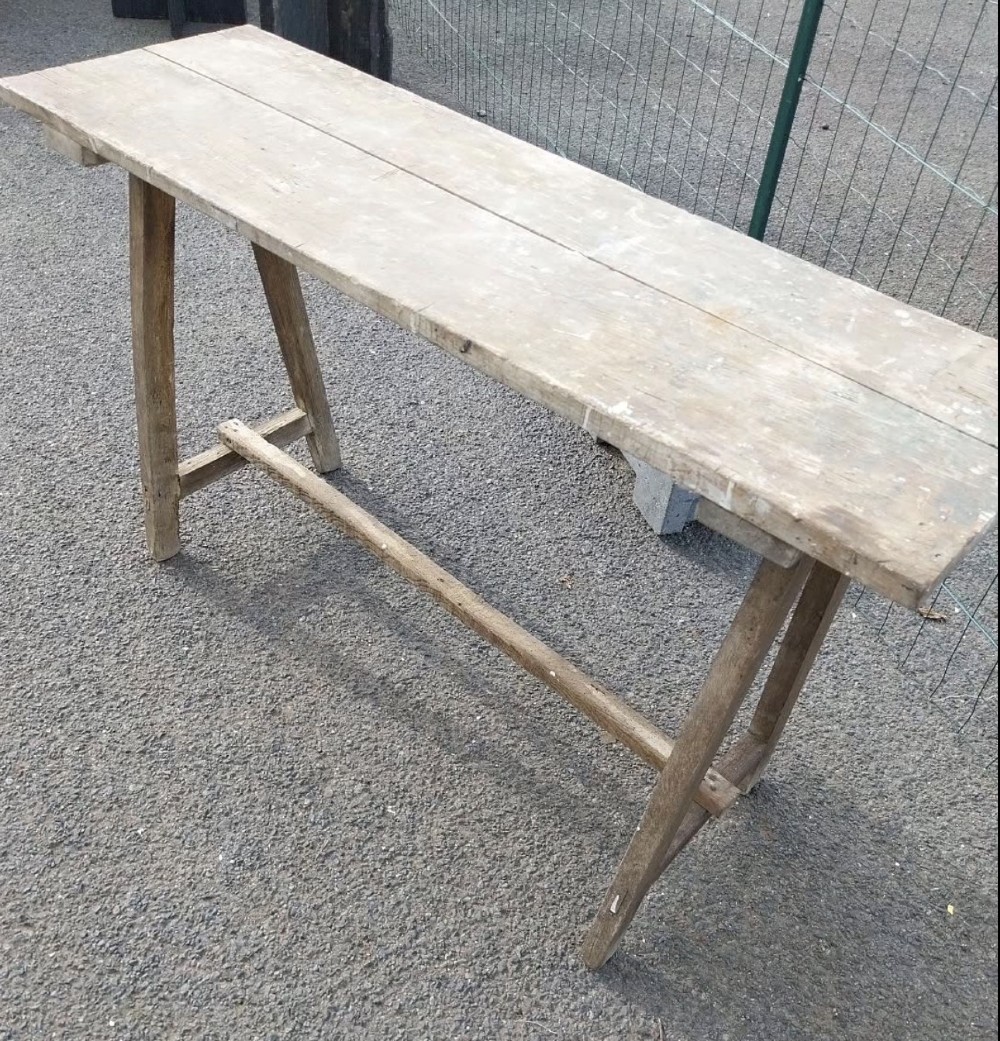 A rustic weathered wooden French laundry table featuring a plank top supported by angled A-frame trestle legs and a central stretcher. View VII