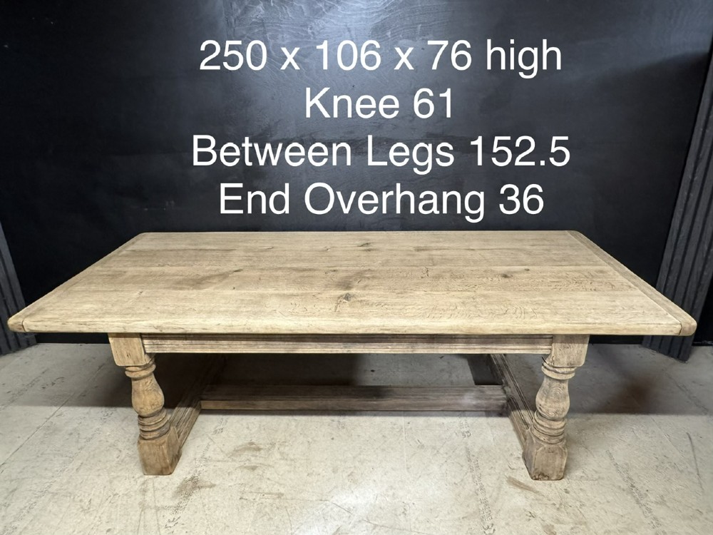 A large natural oak refectory dining table featuring turned legs, breadboard top ends, and an H-stretcher base. View XV