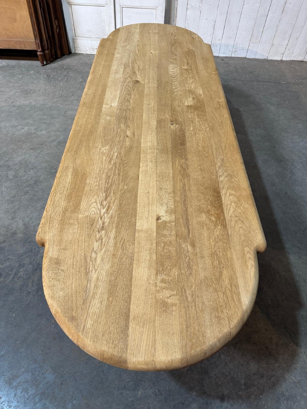 A large rectangular bleached oak dining table featuring carved trestle supports, a central low connecting stretcher, and rounded corner edges. View II