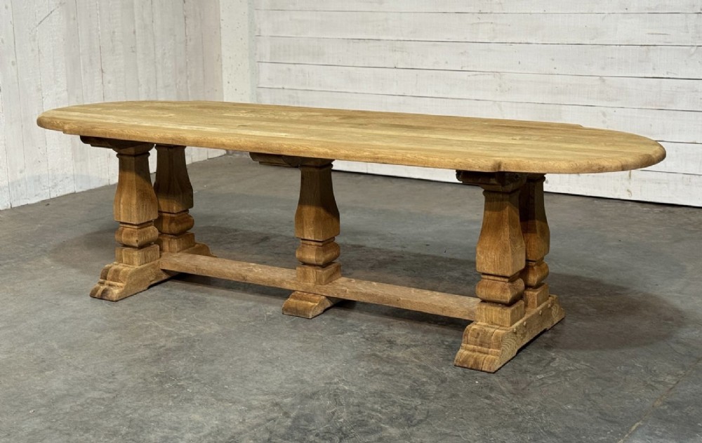 A large rectangular bleached oak dining table featuring carved trestle supports, a central low connecting stretcher, and rounded corner edges. View III