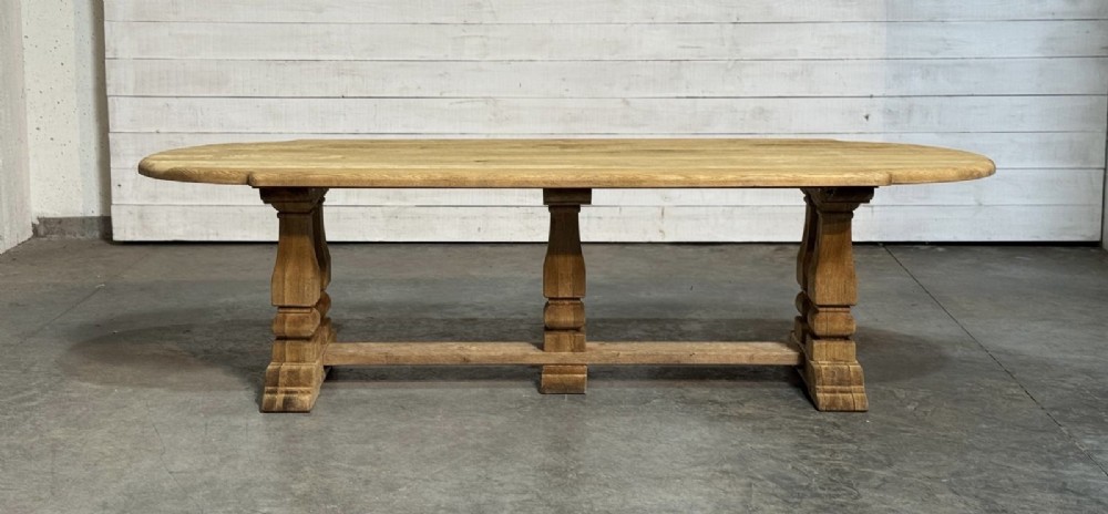 A large rectangular bleached oak dining table featuring carved trestle supports, a central low connecting stretcher, and rounded corner edges. View IV
