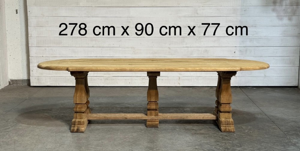 A large rectangular bleached oak dining table featuring carved trestle supports, a central low connecting stretcher, and rounded corner edges. View VII