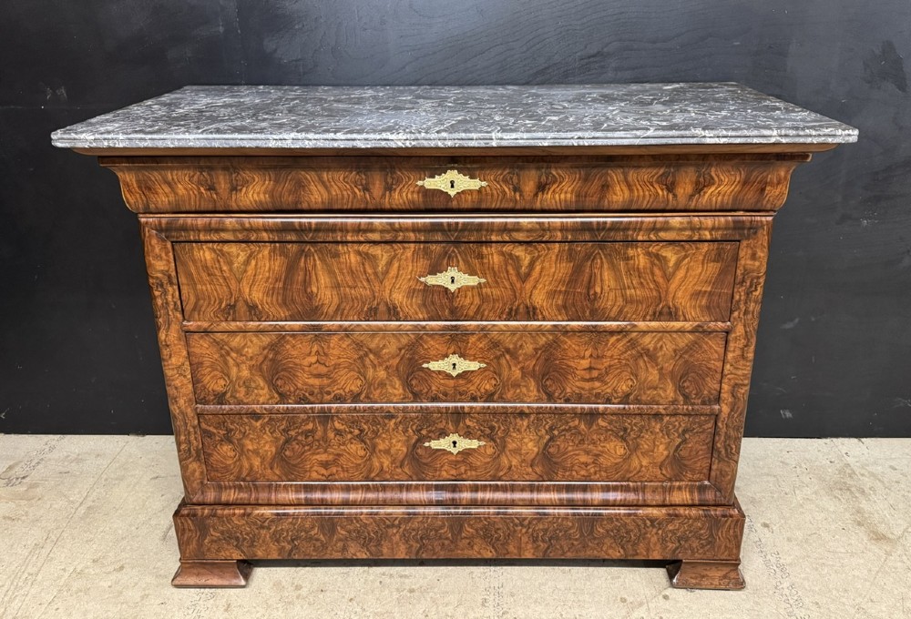 A 19th-century French Louis Philippe burr walnut commode featuring a grey marble top, four drawers, and ornate brass keyhole escutcheons.